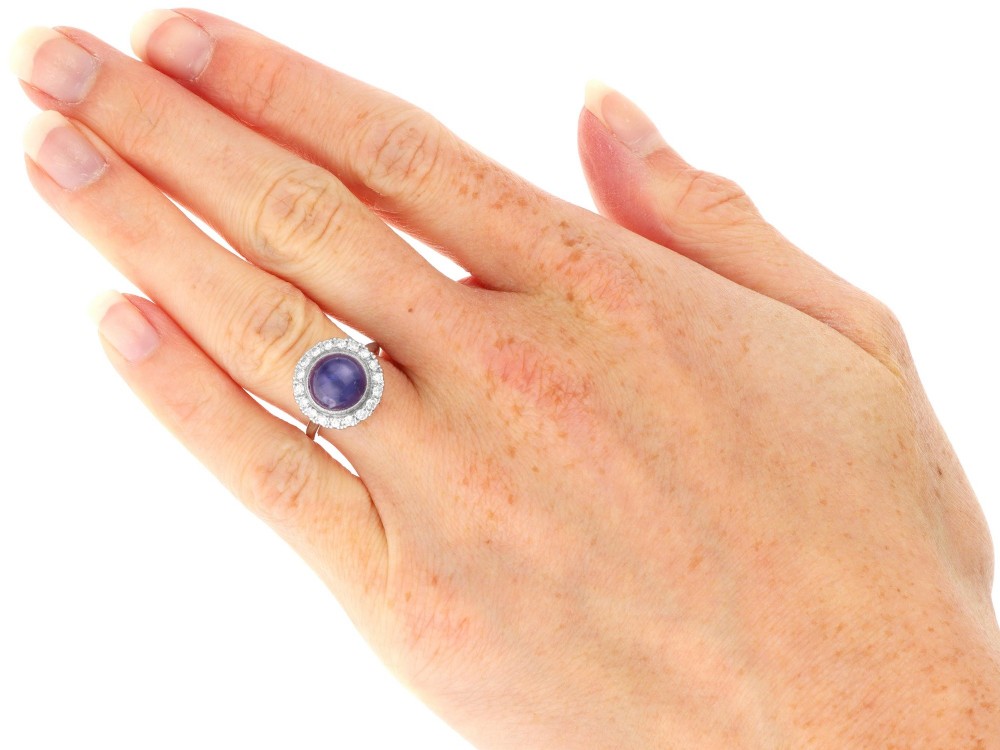 An Art Deco platinum cluster ring featuring a central cabochon star sapphire encircled by a halo of round diamonds with millegrain edging. View XI
