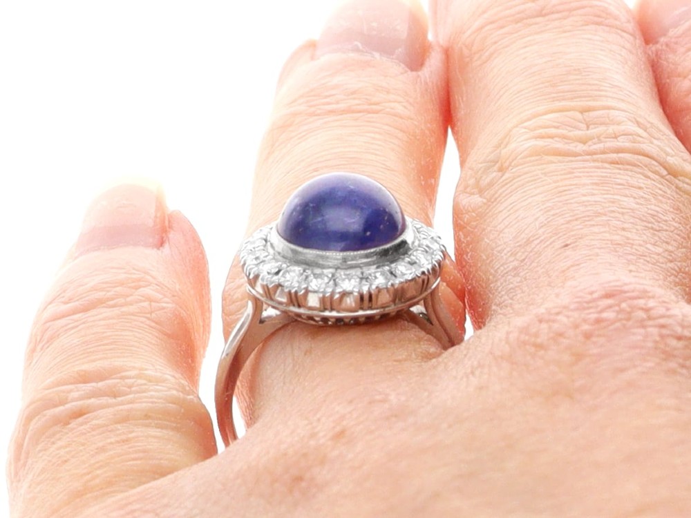 An Art Deco platinum cluster ring featuring a central cabochon star sapphire encircled by a halo of round diamonds with millegrain edging. View XII