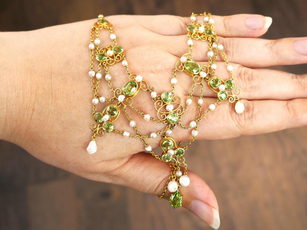 An 18ct yellow gold Belle Epoque festoon necklace featuring faceted green peridots, intricate scrollwork, and suspended natural pearl drops. View III