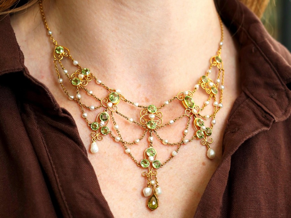 An 18ct yellow gold Belle Epoque festoon necklace featuring faceted green peridots, intricate scrollwork, and suspended natural pearl drops. View IV