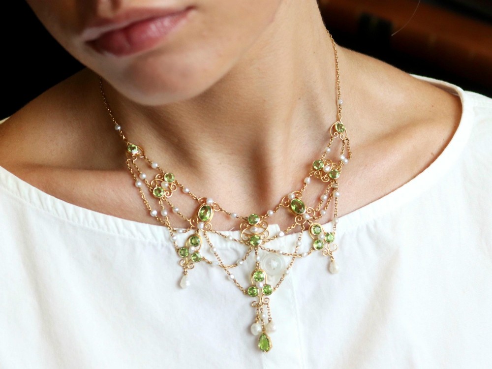 An 18ct yellow gold Belle Epoque festoon necklace featuring faceted green peridots, intricate scrollwork, and suspended natural pearl drops. View V