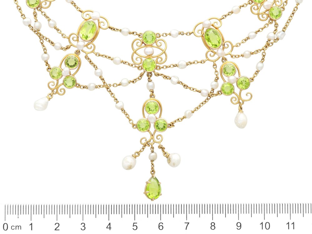 An 18ct yellow gold Belle Epoque festoon necklace featuring faceted green peridots, intricate scrollwork, and suspended natural pearl drops. View X