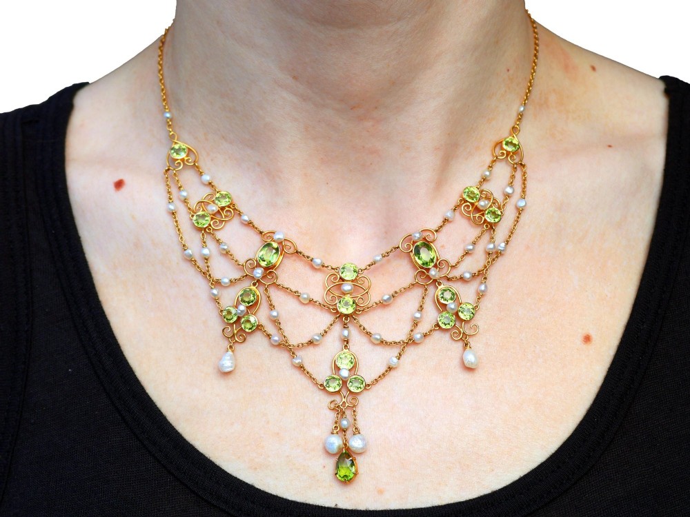 An 18ct yellow gold Belle Epoque festoon necklace featuring faceted green peridots, intricate scrollwork, and suspended natural pearl drops. View XII