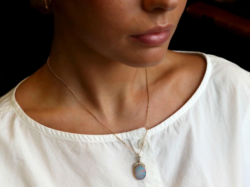 An Edwardian 9ct yellow gold pendant featuring an oval cabochon opal surmounted by millegrain-set diamonds. View IV