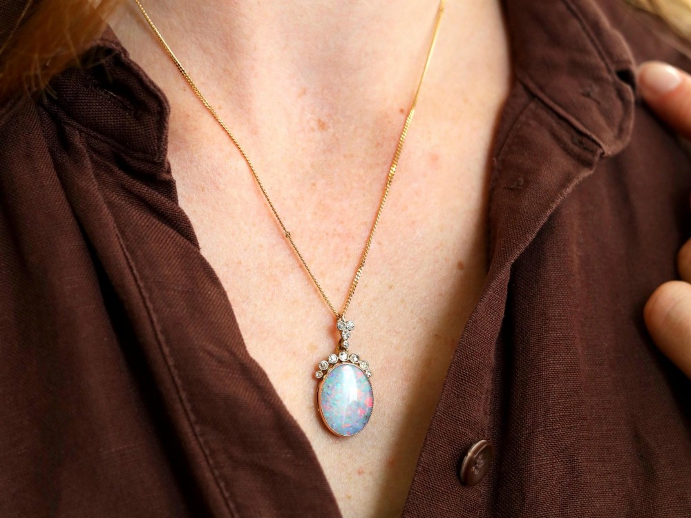An Edwardian 9ct yellow gold pendant featuring an oval cabochon opal surmounted by millegrain-set diamonds. View V