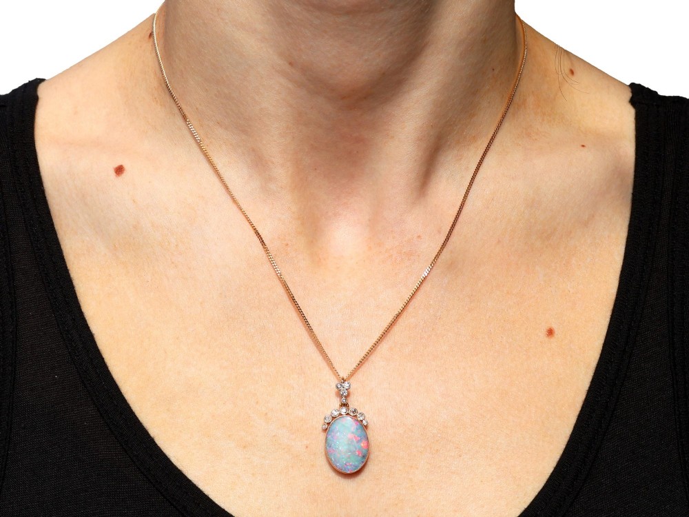 An Edwardian 9ct yellow gold pendant featuring an oval cabochon opal surmounted by millegrain-set diamonds. View XIV