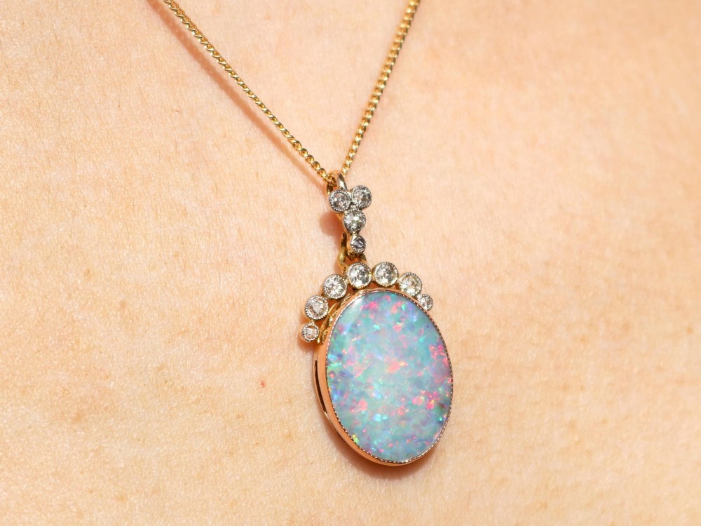 An Edwardian 9ct yellow gold pendant featuring an oval cabochon opal surmounted by millegrain-set diamonds. View XV