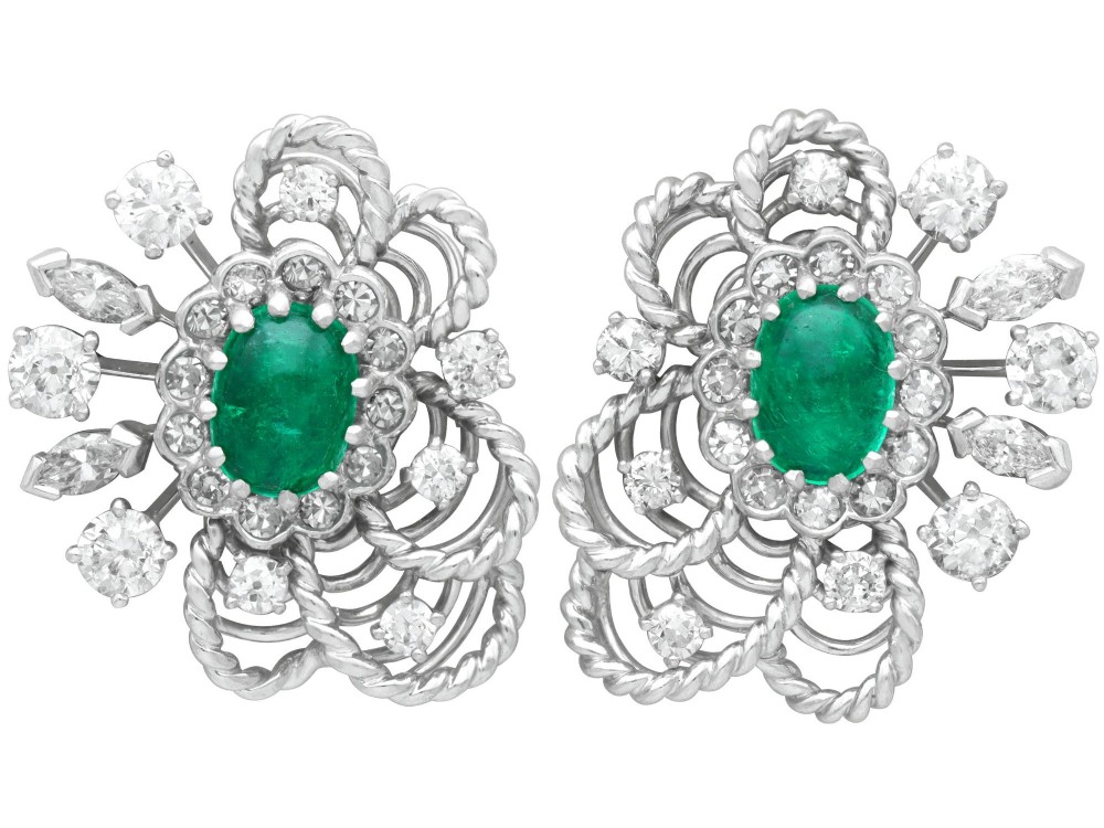 A pair of platinum and palladium clip earrings featuring oval central emeralds surrounded by brilliant-cut diamonds and rope-twist metalwork.