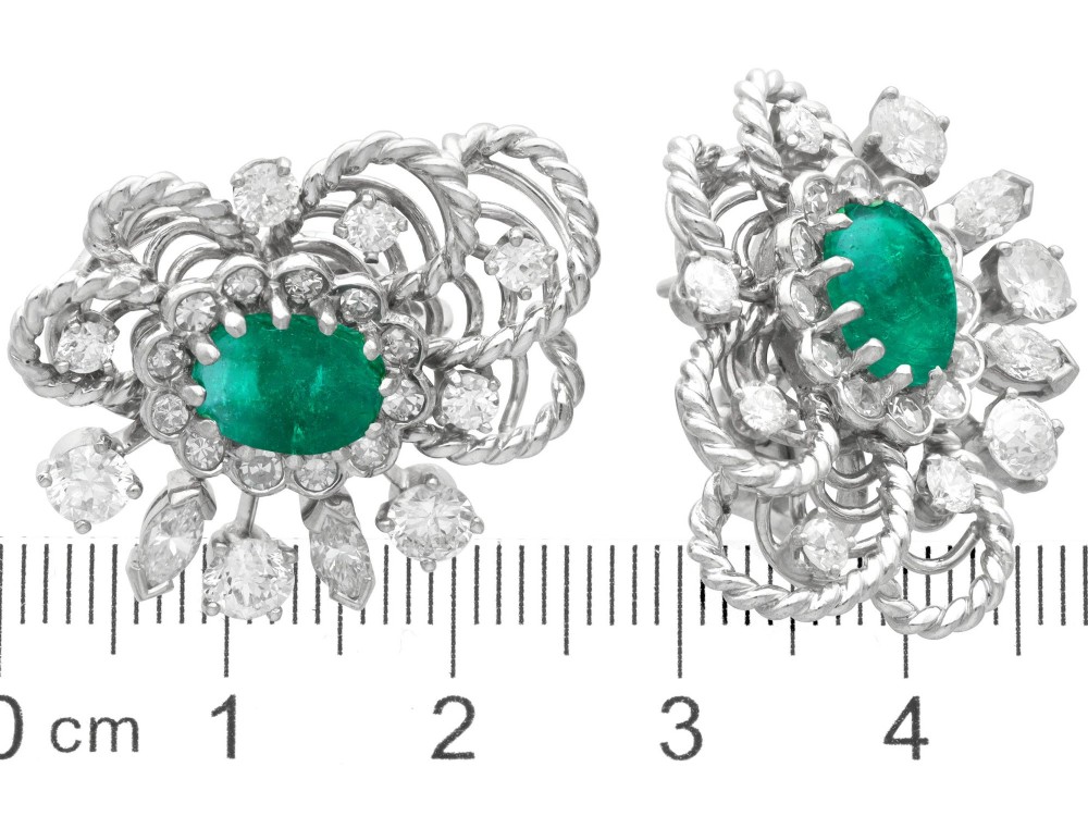 A pair of platinum and palladium clip earrings featuring oval central emeralds surrounded by brilliant-cut diamonds and rope-twist metalwork. View IX