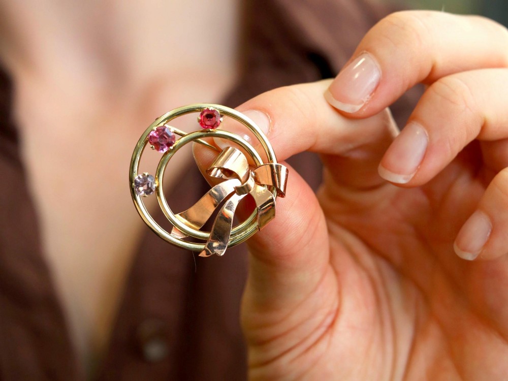 A circular two-tone gold brooch featuring yellow gold concentric rings set with three pink spinels and decorated with a rose gold bow. View III