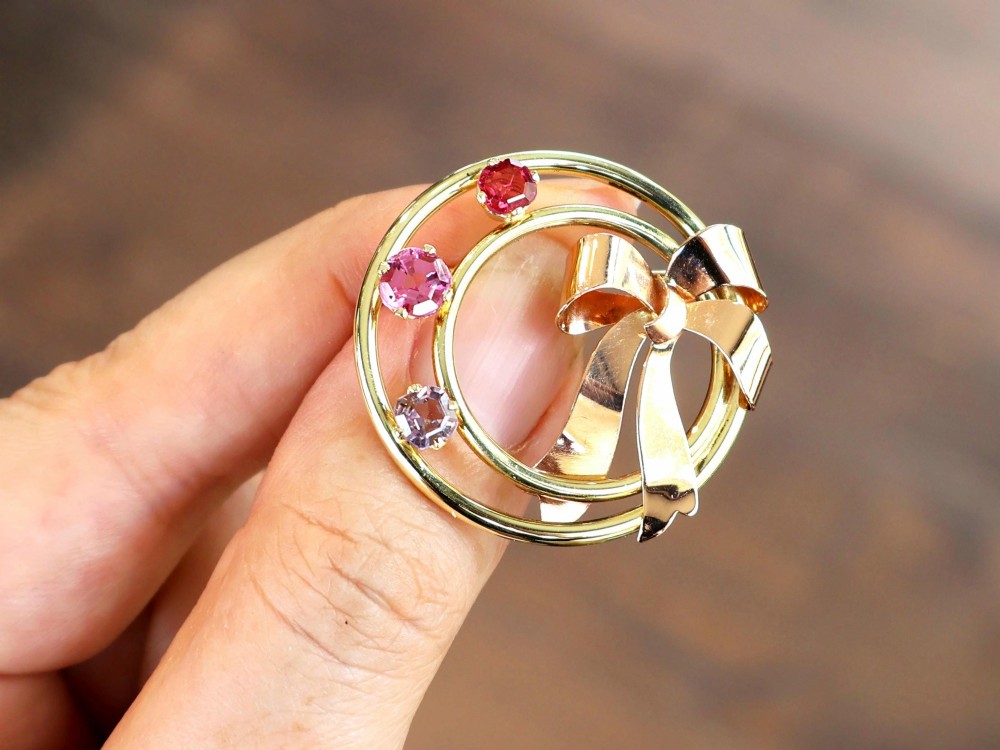A circular two-tone gold brooch featuring yellow gold concentric rings set with three pink spinels and decorated with a rose gold bow. View IV