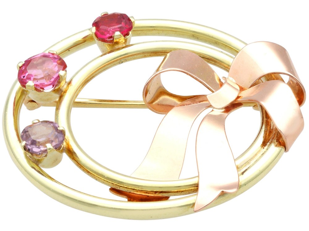 A circular two-tone gold brooch featuring yellow gold concentric rings set with three pink spinels and decorated with a rose gold bow. View X
