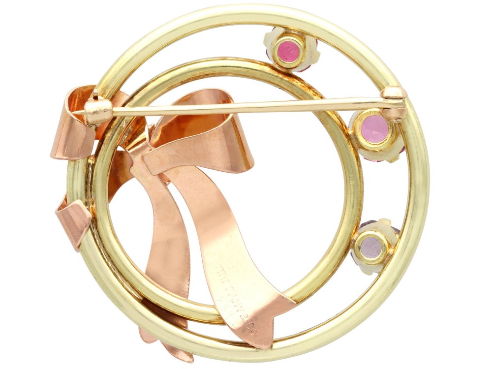 A circular two-tone gold brooch featuring yellow gold concentric rings set with three pink spinels and decorated with a rose gold bow. View XI