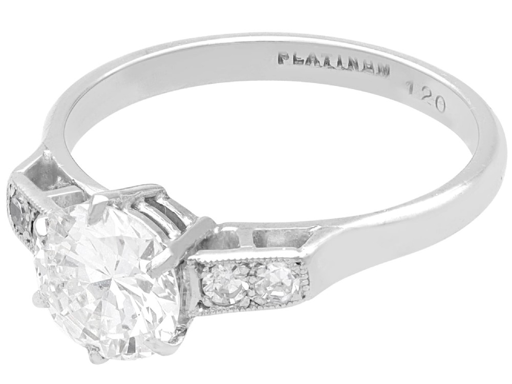 A platinum solitaire ring set with a central round diamond and smaller diamond accents on the shoulders. View VI