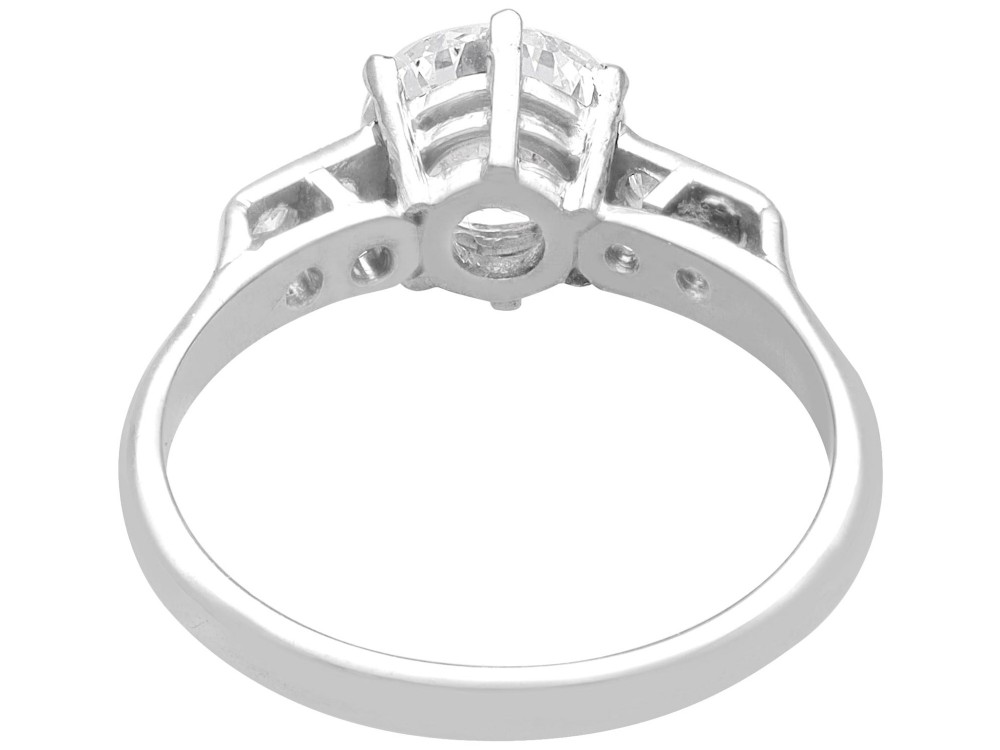A platinum solitaire ring set with a central round diamond and smaller diamond accents on the shoulders. View VII