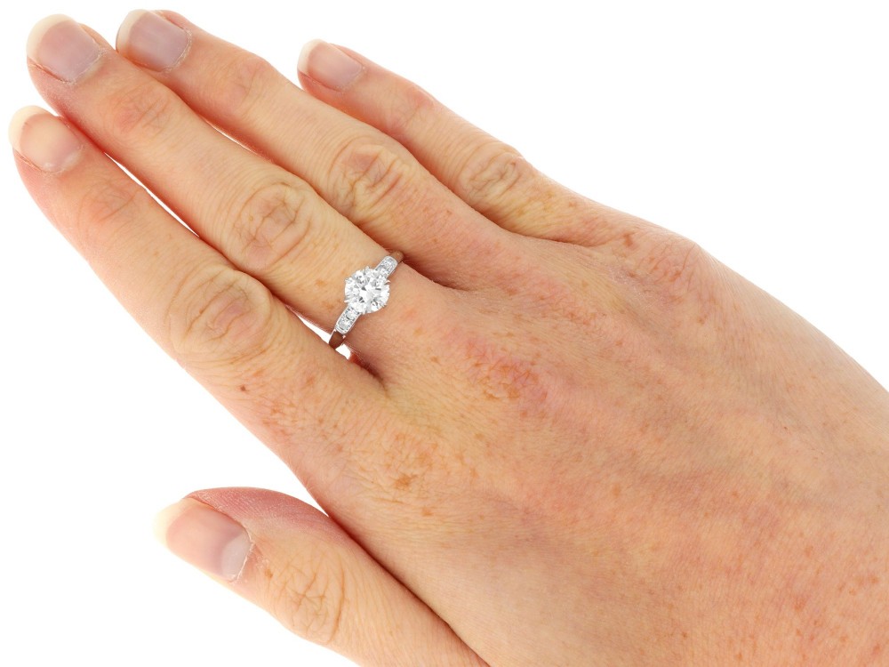 A platinum solitaire ring set with a central round diamond and smaller diamond accents on the shoulders. View IX