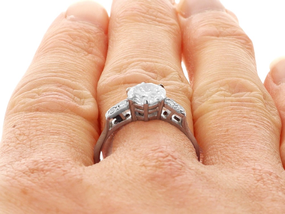 A platinum solitaire ring set with a central round diamond and smaller diamond accents on the shoulders. View XI