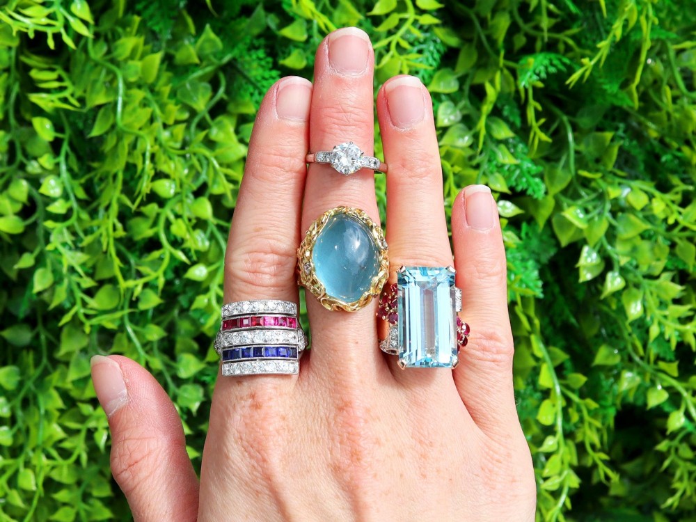 An antique platinum ring displaying horizontal rows of round diamonds alternating with channel-set rectangular blue sapphires and red rubies. View III