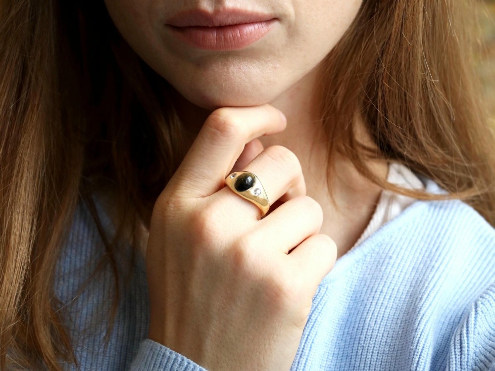 An 18ct yellow gold ring set with a central oval cabochon tigers eye stone flanked by two flush-set diamonds. View IV