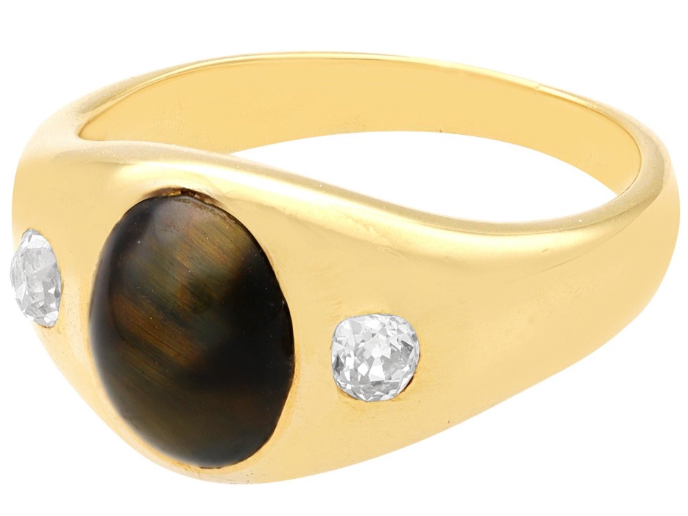 An 18ct yellow gold ring set with a central oval cabochon tigers eye stone flanked by two flush-set diamonds. View V