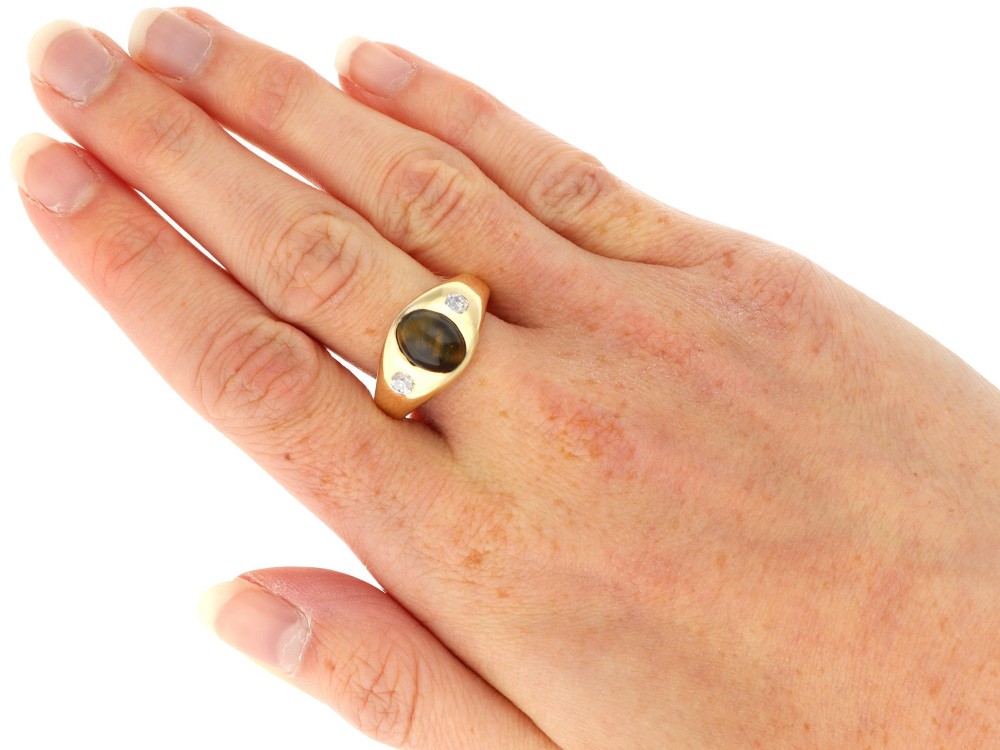 An 18ct yellow gold ring set with a central oval cabochon tigers eye stone flanked by two flush-set diamonds. View IX