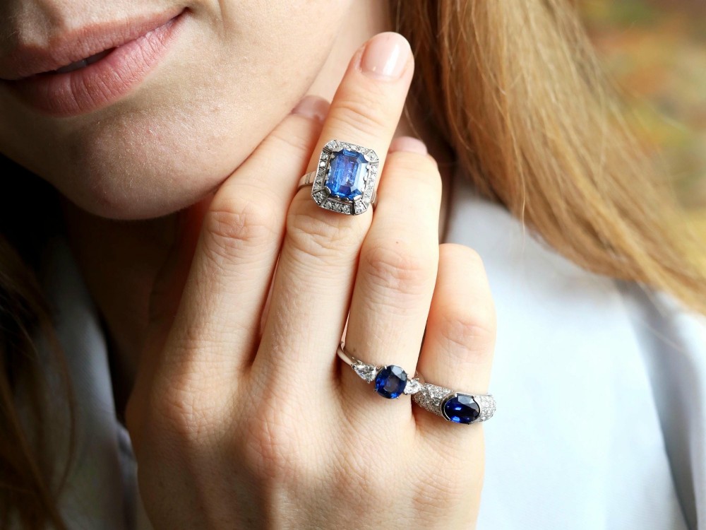 An Art Deco 18ct white gold ring featuring a central octagonal step-cut blue Ceylon sapphire surrounded by a geometric diamond halo with milgrain details. View III