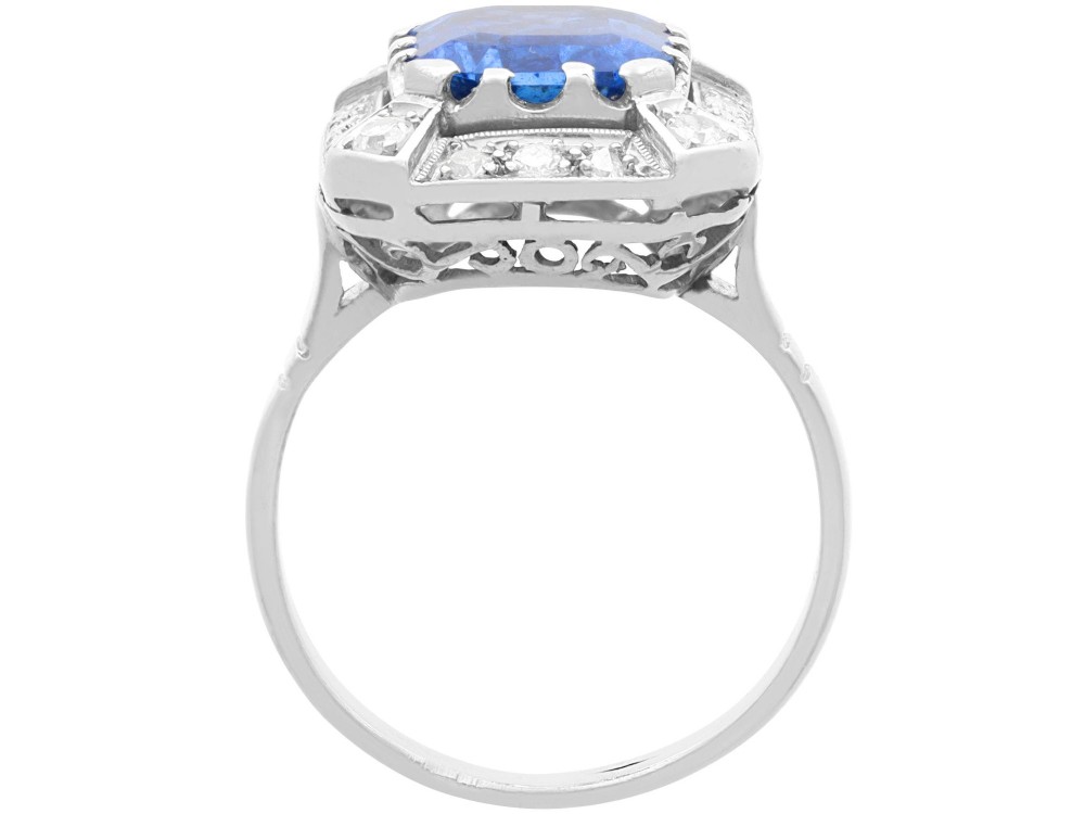 An Art Deco 18ct white gold ring featuring a central octagonal step-cut blue Ceylon sapphire surrounded by a geometric diamond halo with milgrain details. View VIII