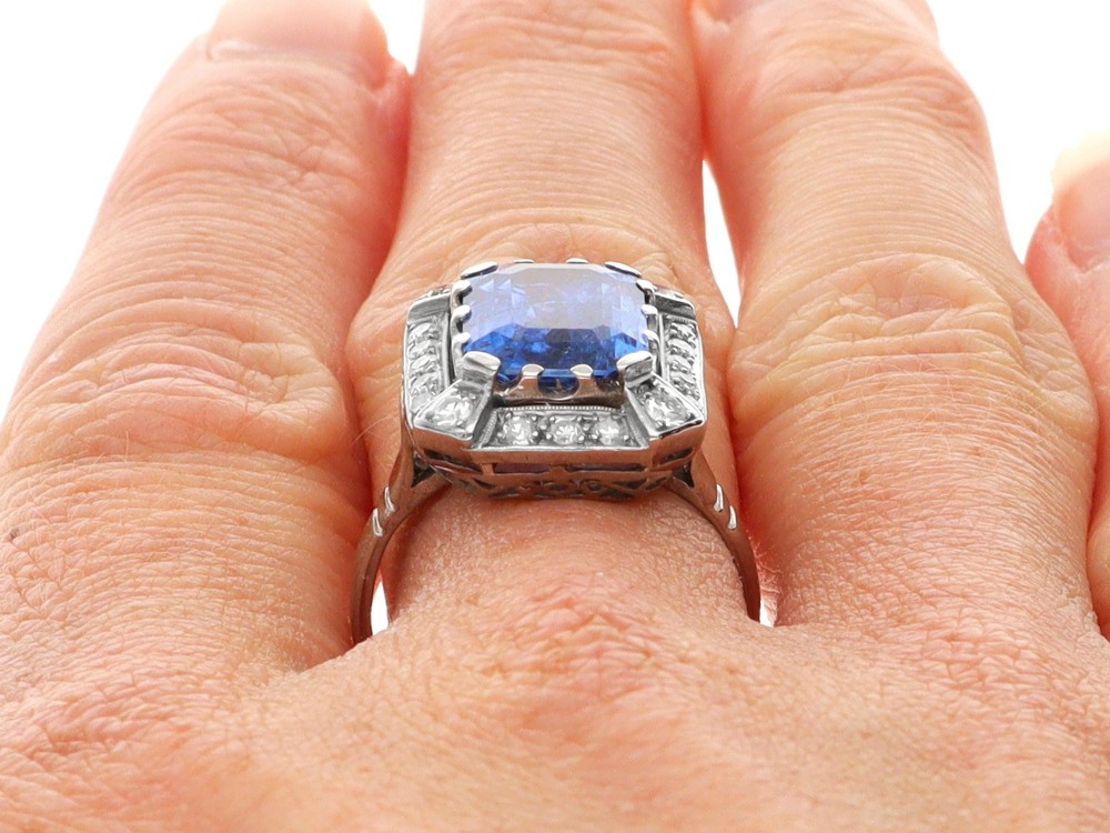 An Art Deco 18ct white gold ring featuring a central octagonal step-cut blue Ceylon sapphire surrounded by a geometric diamond halo with milgrain details. View XI