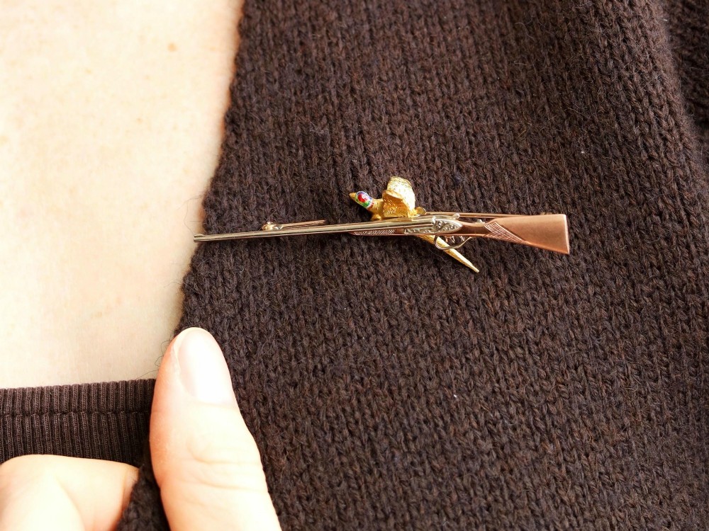 A vintage 9ct gold brooch depicting a flying pheasant with a red and green enamelled head positioned alongside a shotgun. View V