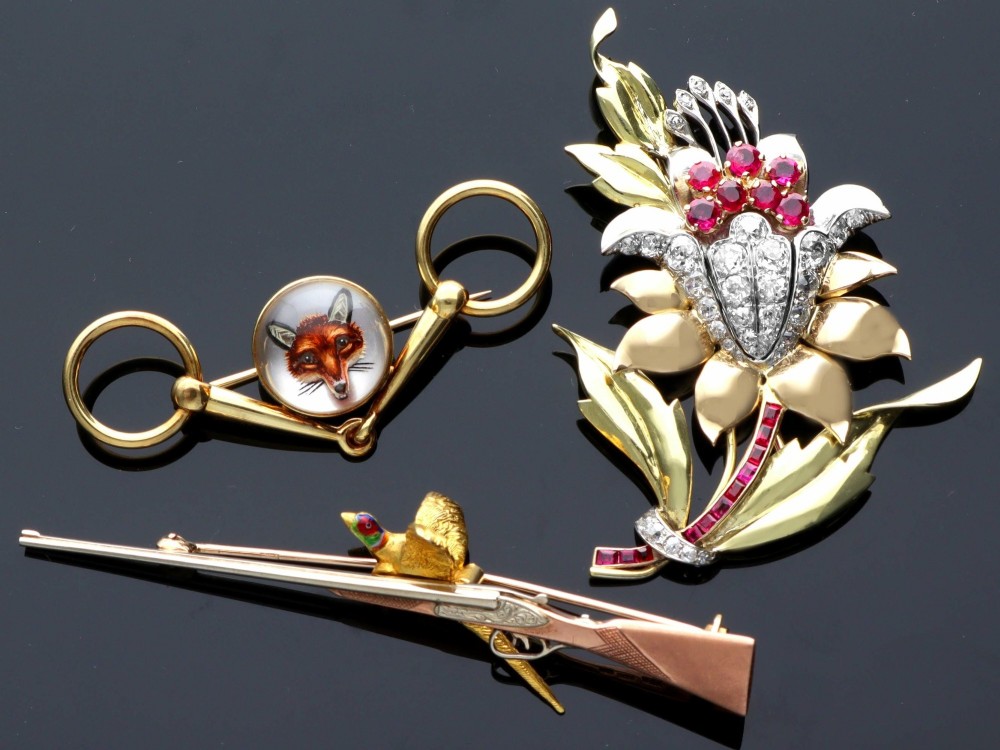 A vintage 9ct gold brooch depicting a flying pheasant with a red and green enamelled head positioned alongside a shotgun. View VI
