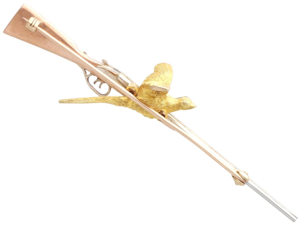 A vintage 9ct gold brooch depicting a flying pheasant with a red and green enamelled head positioned alongside a shotgun. View XI