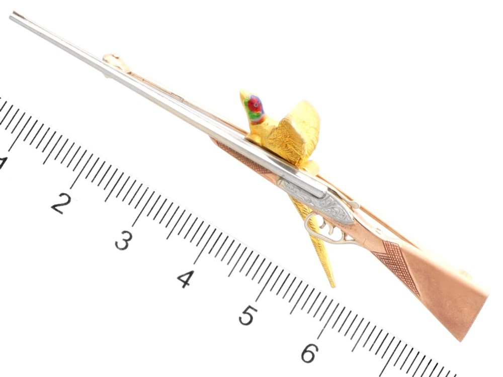 A vintage 9ct gold brooch depicting a flying pheasant with a red and green enamelled head positioned alongside a shotgun. View XII