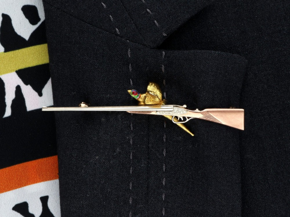 A vintage 9ct gold brooch depicting a flying pheasant with a red and green enamelled head positioned alongside a shotgun. View XIII
