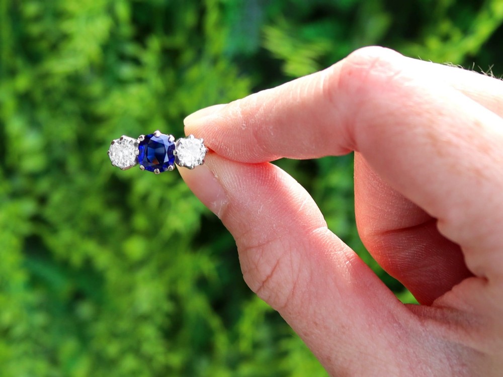 An antique 18ct yellow gold trilogy ring featuring a cushion-shaped blue sapphire flanked by two brilliant-cut diamonds in claw settings. View II