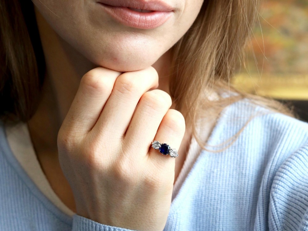 An antique 18ct yellow gold trilogy ring featuring a cushion-shaped blue sapphire flanked by two brilliant-cut diamonds in claw settings. View VI