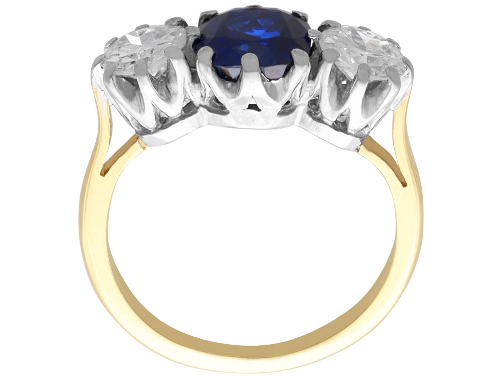 An antique 18ct yellow gold trilogy ring featuring a cushion-shaped blue sapphire flanked by two brilliant-cut diamonds in claw settings. View X