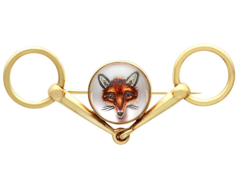 An antique 14ct yellow gold brooch designed as an equestrian snaffle bit with a central round reverse intaglio rock crystal depicting a painted fox mask.