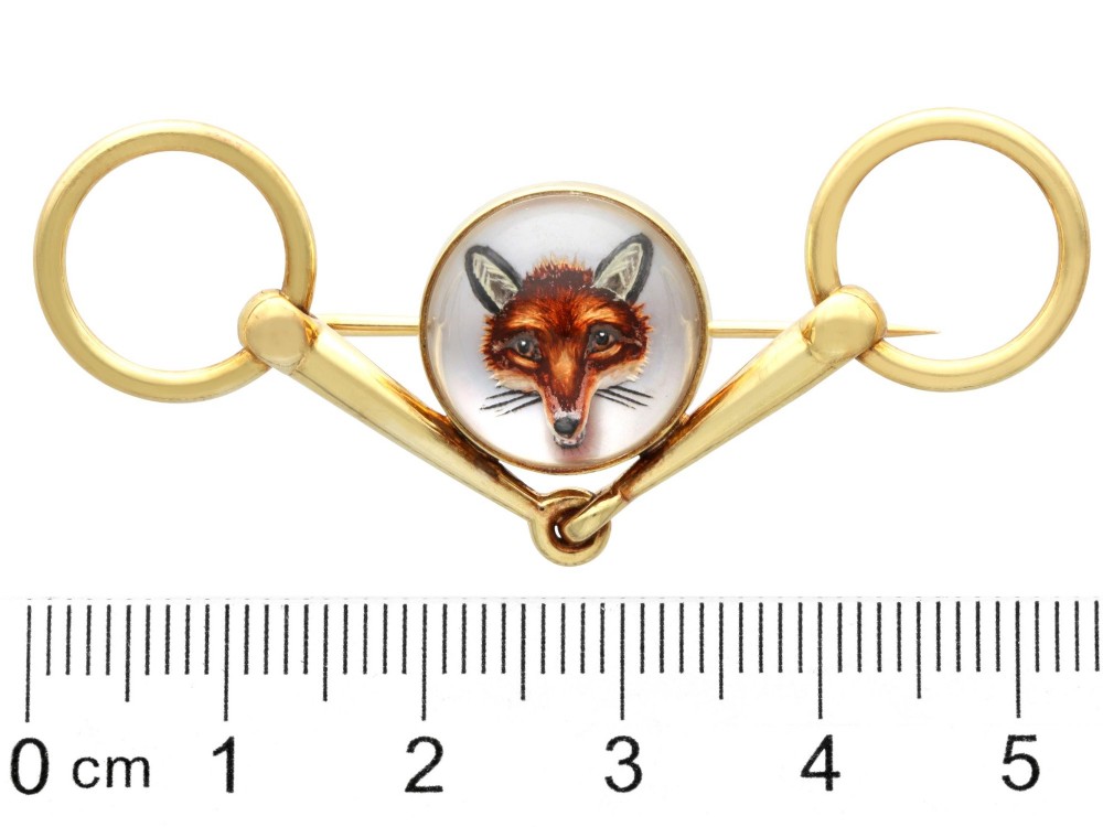 An antique 14ct yellow gold brooch designed as an equestrian snaffle bit with a central round reverse intaglio rock crystal depicting a painted fox mask. View IX