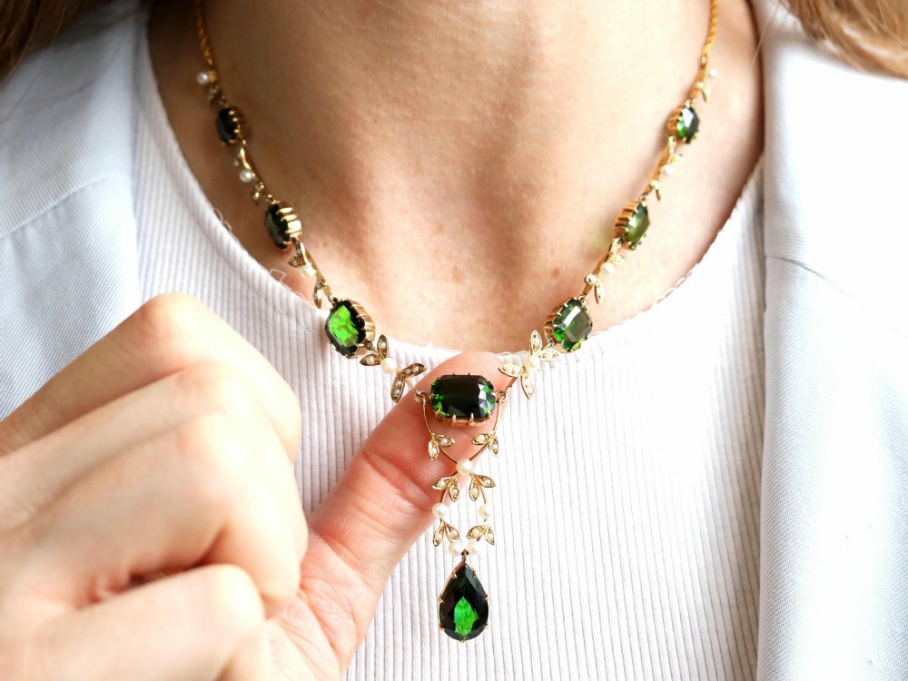 A late Victorian 14ct yellow gold necklace featuring emerald-cut green tourmalines connected by seed pearl foliate links and terminating in a pear-cut green tourmaline drop pendant. View IV