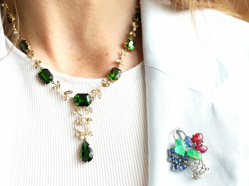 A late Victorian 14ct yellow gold necklace featuring emerald-cut green tourmalines connected by seed pearl foliate links and terminating in a pear-cut green tourmaline drop pendant. View V