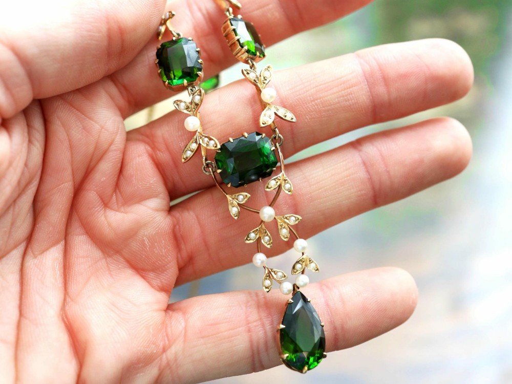 A late Victorian 14ct yellow gold necklace featuring emerald-cut green tourmalines connected by seed pearl foliate links and terminating in a pear-cut green tourmaline drop pendant. View VIII