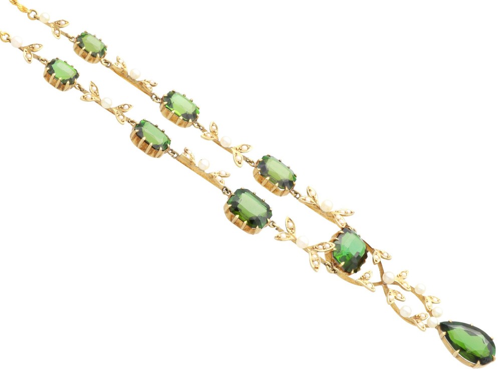 A late Victorian 14ct yellow gold necklace featuring emerald-cut green tourmalines connected by seed pearl foliate links and terminating in a pear-cut green tourmaline drop pendant. View X