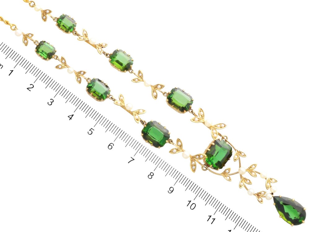 A late Victorian 14ct yellow gold necklace featuring emerald-cut green tourmalines connected by seed pearl foliate links and terminating in a pear-cut green tourmaline drop pendant. View XII