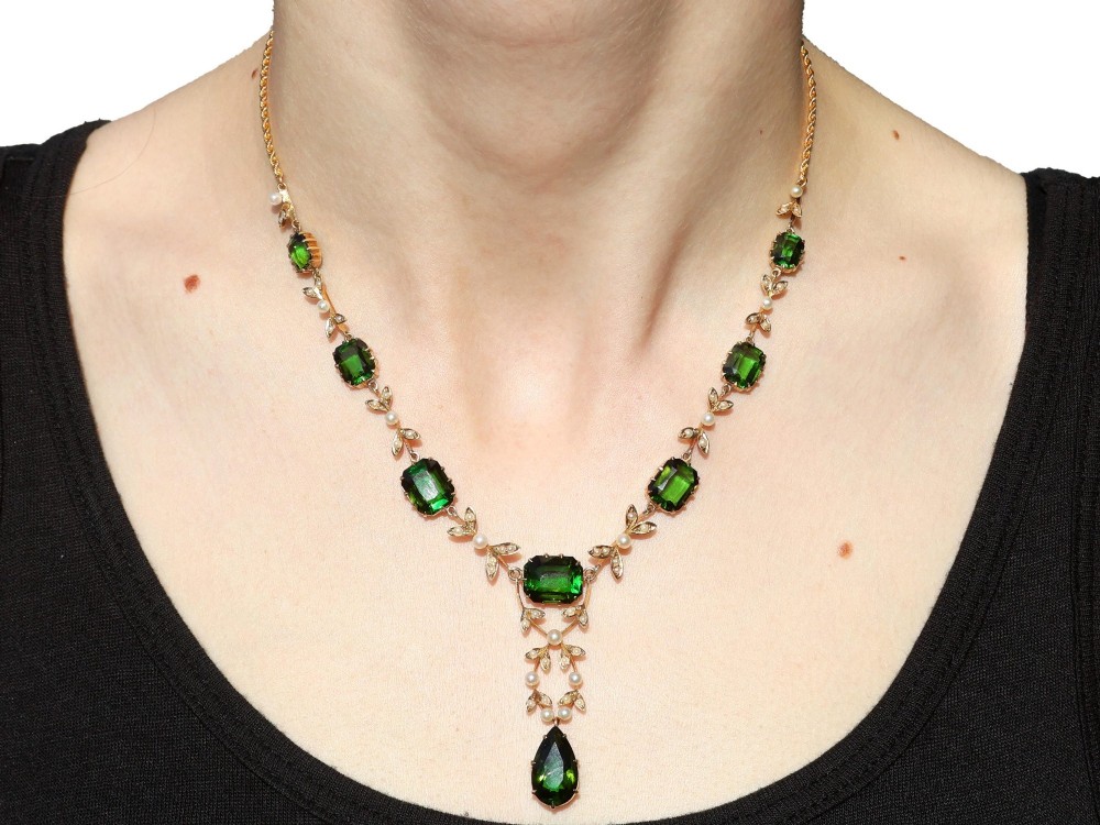A late Victorian 14ct yellow gold necklace featuring emerald-cut green tourmalines connected by seed pearl foliate links and terminating in a pear-cut green tourmaline drop pendant. View XIV