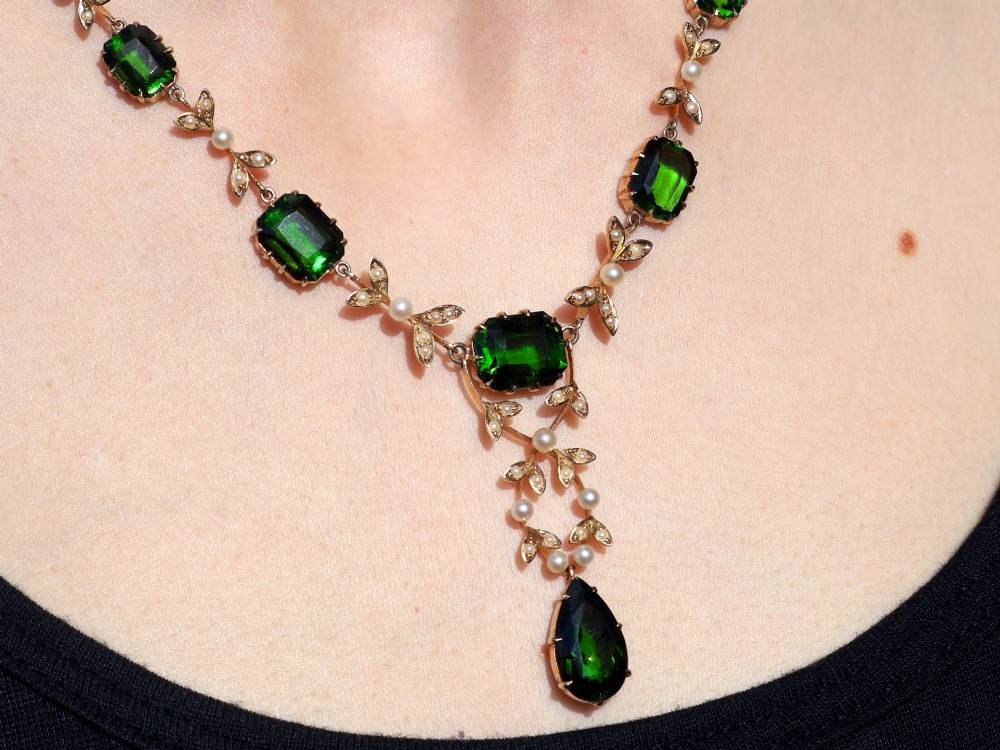 A late Victorian 14ct yellow gold necklace featuring emerald-cut green tourmalines connected by seed pearl foliate links and terminating in a pear-cut green tourmaline drop pendant. View XV