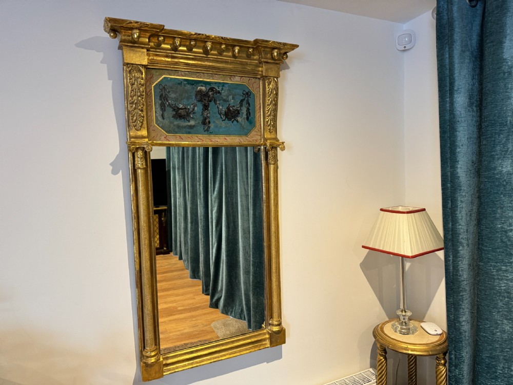 An early 19th-century Regency giltwood pier mirror featuring reeded side pilasters, a ball-encrusted cornice, and a decorative reverse-painted verre eglomise top panel.