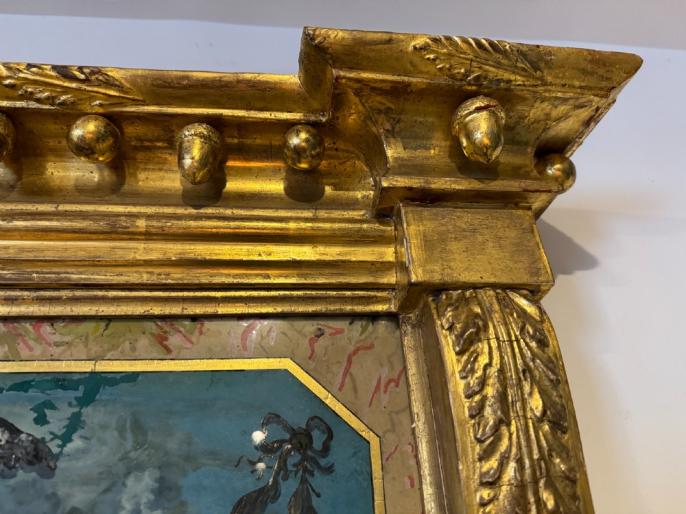 An early 19th-century Regency giltwood pier mirror featuring reeded side pilasters, a ball-encrusted cornice, and a decorative reverse-painted verre eglomise top panel. View IV