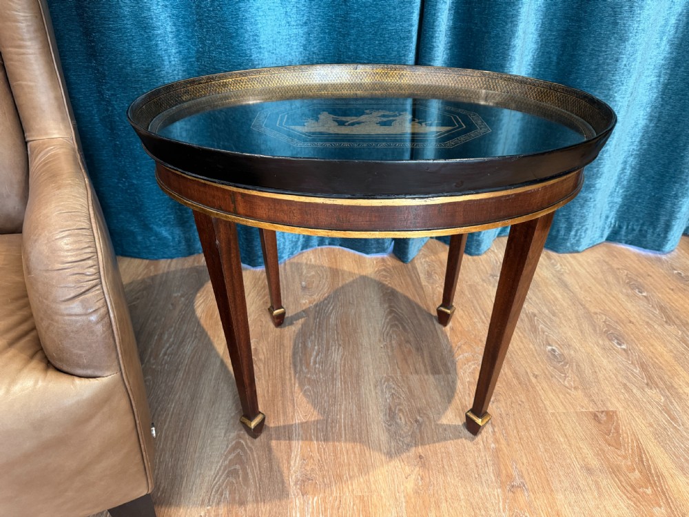 An early 19th-century oval tray table featuring a black lacquered top with gilded classical decoration on tapered mahogany legs.
