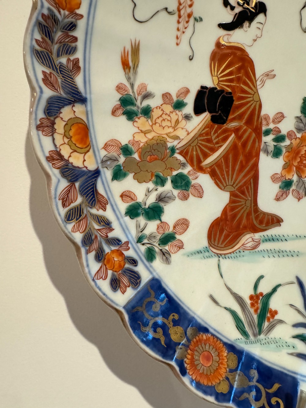 A large Japanese Meiji period porcelain charger plate with a scalloped edge, depicting women in traditional kimonos beneath a tree, bordered in cobalt blue and floral motifs. View II