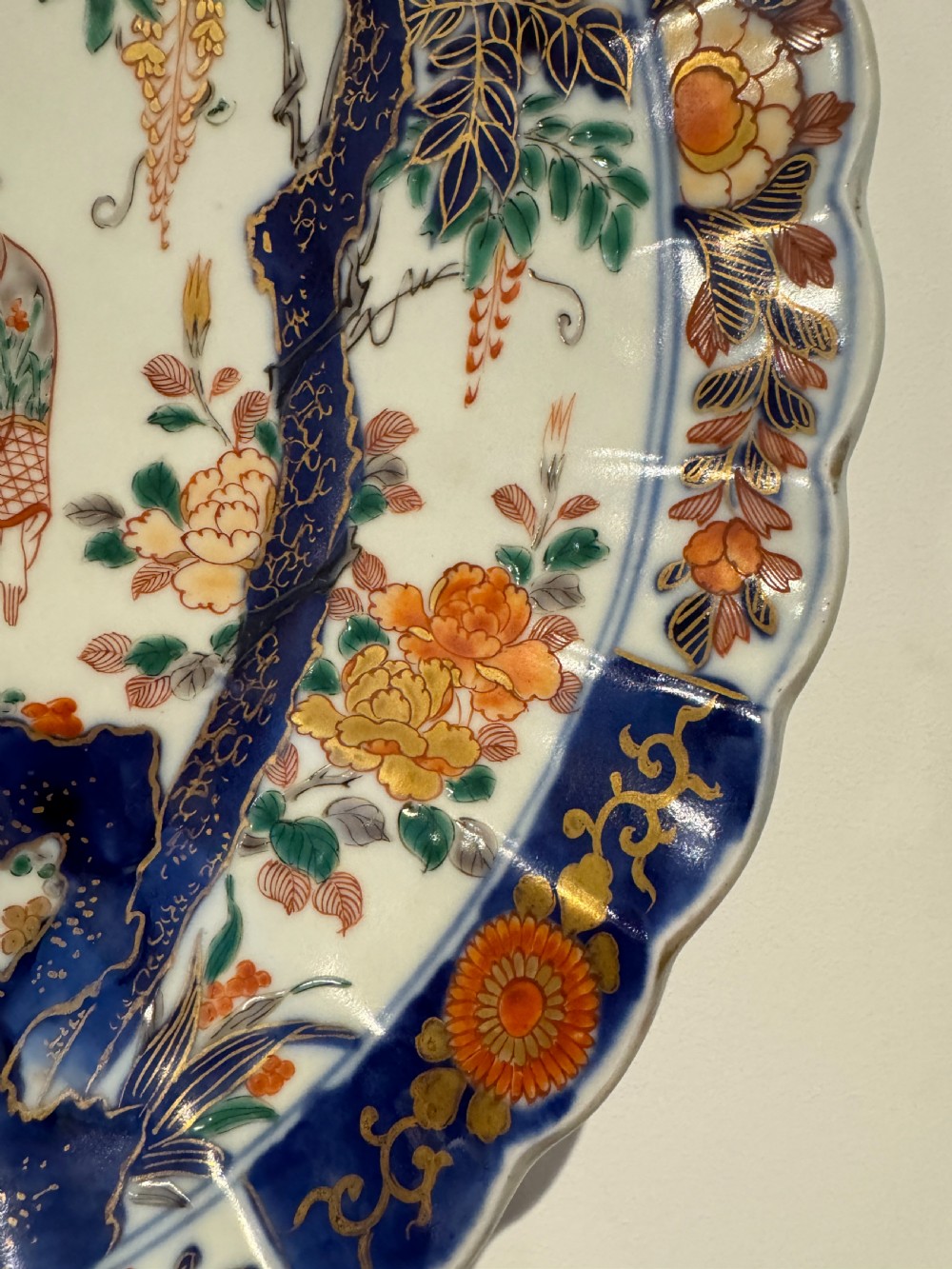 A large Japanese Meiji period porcelain charger plate with a scalloped edge, depicting women in traditional kimonos beneath a tree, bordered in cobalt blue and floral motifs. View III